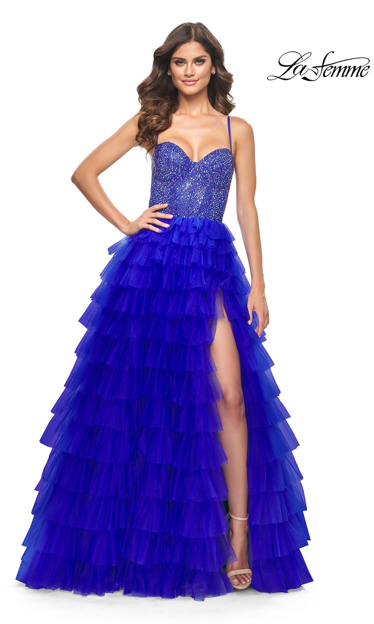 Woman modeling the La Femme Long Ruffled Prom Ball Gown 32002 in royal blue, featuring a beaded bodice, thin straps, and a thigh-high slit, with one hand on her hip.